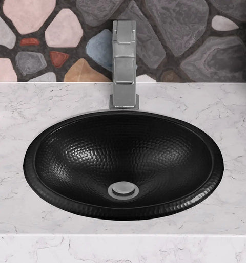 Overhead view of the 17 Inch Oval Drop In Matte Black Bathroom Sink With Hand Hammered Finish, mounted on a marble countertop.