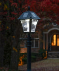 Baytown II Outdoor Solar Lamp Post with EZ Anchor Kit, Black Finish, illuminating at dusk in a garden with autumn leaves.
