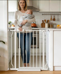 Woman holding baby near adjustable narrow baby gate fits 24 to 29 inches wide pressure mounted no drill walk through metal safety gate.