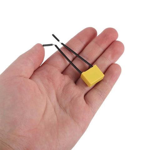 Get Your Hands On 30 Pcs Of High Voltage Microfarad Safety Capacitors With Built In Wire And Plastic Casing For Rock Solid Electrical Appliance Testing And Maintenance Work Without The Headache Or Risky Failures - Yellow capacitor on a hand.