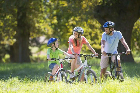 Family biking through park trail, wearing helmets and casual clothes on sunny day
