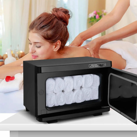 Pro 8L Towel Warmer For Salon And Spa in black, filled with rolled towels, next to a woman receiving a back massage in a spa setting.