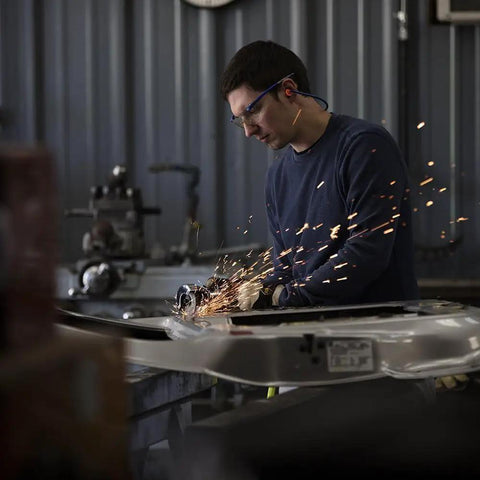 Worker using Heavy Duty Sixty Gallon Two Stage Air Compressor during metal grinding, sparks flying in workshop.
