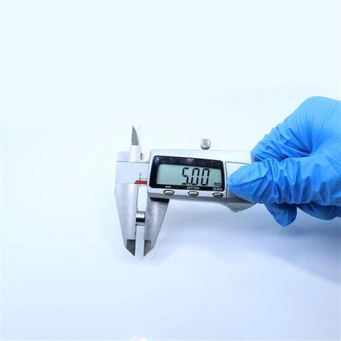 Digital caliper measuring 5.00 mm size in hand with a blue glove over a plain background for precise measurement of small objects.