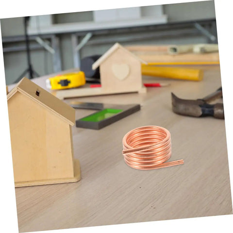 Copper coil on a table with wooden models and tools, part of Water Cooling Jacket Kit For Brush Boat Motors And Copper Ring Cooling Ring RC Boat Toy Accessory 550 Size Brush Motor Compatible Easy Install Keeps Your Motor Chill For Peak Performance And Long Life.