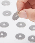 Stainless steel fender washer held between fingers; flat disc with central hole, with several washers on white background.