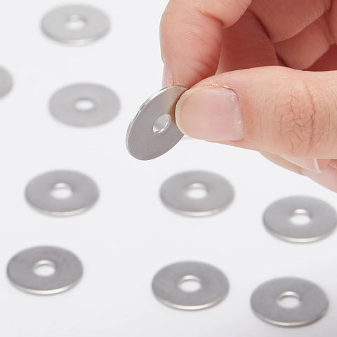 Stainless steel fender washer held between fingers; flat disc with central hole, with several washers on white background.
