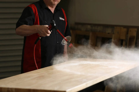 Person using Heavy Duty Aluminum Die Cast High Flow Air Blow Gun Master Set with 3 Nozzles and Debris Shield to clear table surface.