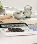 Desktop calculator with coffee cup, alarm clock, and open notebook on a light marble surface