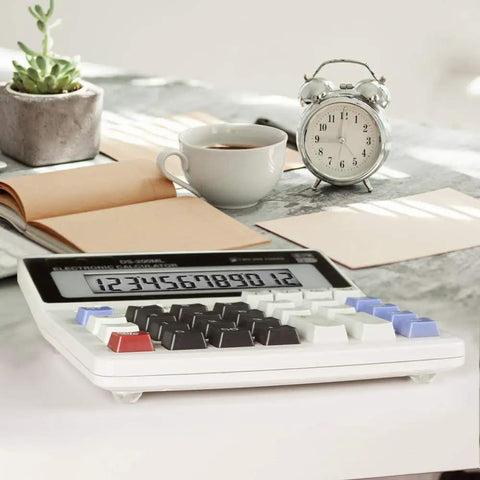 Desktop calculator with coffee cup, alarm clock, and open notebook on a light marble surface