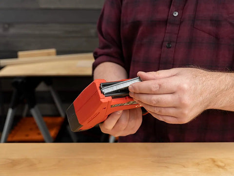 Person holding Cordless And Battery Powered Go To 5 In 1 Staple And Nail Gun, inserting T50 staple, workbench in background