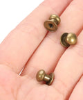 36 Pack Mini Round Knobs With An Upscale Bronze Touch Forged From Tough Zinc Alloy held in a hand, showcasing compact size and bronze finish.