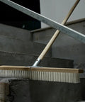 Heavy Duty Push Broom With Rock Solid Four Layer Stiff Plastic Bristles And A Beefy Wooden Handle cleaning concrete steps.