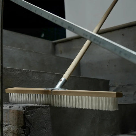 Heavy Duty Push Broom With Rock Solid Four Layer Stiff Plastic Bristles And A Beefy Wooden Handle cleaning concrete steps.