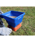 Person using handheld grass seed and fertilizer spreader for lawns and driveways lightweight and corrosion resistant with ergonomic grip