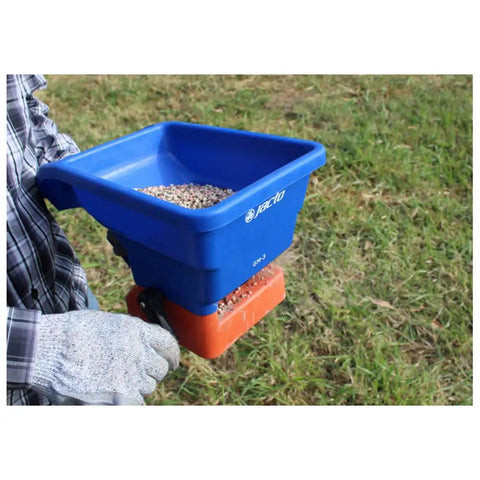 Person using handheld grass seed and fertilizer spreader for lawns and driveways lightweight and corrosion resistant with ergonomic grip