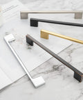 Assorted metallic cabinet pull handles arranged on marble surface, various finishes, different sizes and styles.