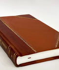 Leather-bound brown book with gold-foil spine and edge detailing, thick white pages.