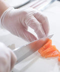 Straight Up Premium Clear Vinyl Exam Gloves Large 1000 Pack Latex Free Powder Free used for slicing salmon in a kitchen setting.