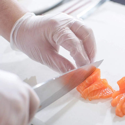 Straight Up Premium Clear Vinyl Exam Gloves Large 1000 Pack Latex Free Powder Free used for slicing salmon in a kitchen setting.