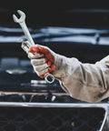 Mechanic holding a wrench with red gloves near a car engine under maintenance.