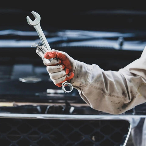 Mechanic holding a wrench with red gloves near a car engine under maintenance.
