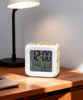 Compact Digital Alarm Clock With Cute Sunflower Butterfly Cube Shape Silent Sweep Motor And Soft Led Glow Includes Built In Snooze Button Shows Time Date And Room Temp on wooden desk with laptop.