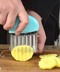 Front view of blue plastic-handled stainless steel crinkle cutter slicing a potato on a cutting board.