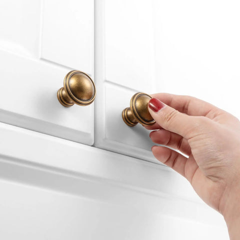 Hand installing Ten Pack One And One Quarter Inch Antique Brass Kitchen Cabinet Knobs For Cabinets Drawers Dresser Cupboard Bedroom And Bathroom Hardware Real Solid Metal Vintage Brass Knob Set With Classic Look Built To Last on white cabinet.