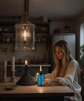 Woman sitting at table with blue glass torch, part of 4 Pack Glass Table Top Torches With Wick And Cap, Multicolor Citronella Lanterns.