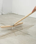 Heavy Duty Push Broom With Rock Solid Four Layer Stiff Plastic Bristles And A Beefy Wooden Handle for cleaning a concrete floor.