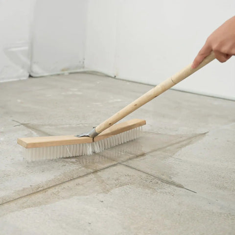 Heavy Duty Push Broom With Rock Solid Four Layer Stiff Plastic Bristles And A Beefy Wooden Handle for cleaning a concrete floor.
