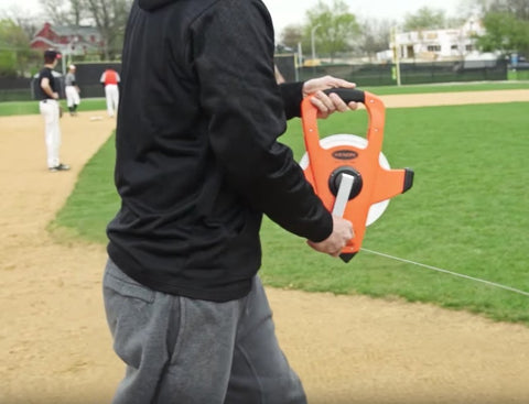 Person using NRS18M330 Nylon Reinforced Tape Measure With Beast Speed Rewind And Double Hook 100M on a sports field
