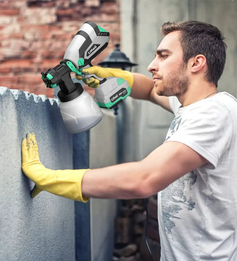 Person using 20V Cordless HVLP Paint Sprayer Gun With 4.0 Ah Battery And Charger, applying paint on concrete surface outdoors.