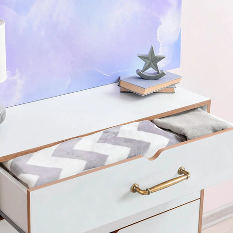Open drawer with antique brass cabinet handle, featuring chevron-patterned blanket and decorative items on top, showcasing usage.