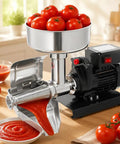 Heavy Duty Electric Tomato Sauce Maker And Fruit Strainer with stainless steel funnel, tomatoes, and tomato puree on a wooden counter.
