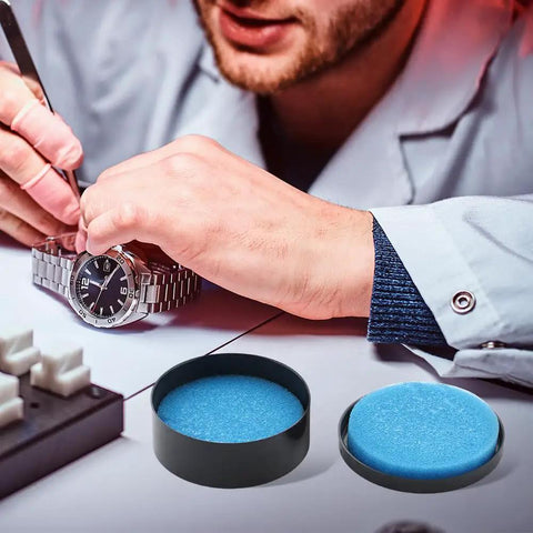Watchmaker repairing watch near Pro Grade Watch Gasket Grease Silicone Lubricant For O-Rings And Case Backs, visible in black and blue.