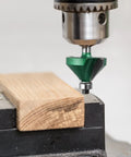 Pro Router Bit Set 40-Piece Carbide Bits For Woodworking attached to a drill press, shaping a wooden plank with precision.
