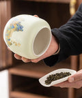 Top Shelf Ceramic Tea Tin With Woven Rattan Travel Case, Stunning Mountain Landscape Design, Go To Stash Jar For Loose Leaf Tea Or Specialty Coffee Beans In Slate Blue held while pouring loose leaf tea.