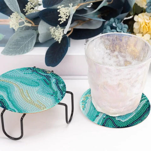 Diamond Art Coaster Set With Holder For DIY Craft Lovers, 8 teal marble coasters with cork pads displayed with a glass on one.