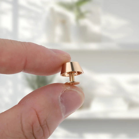 Top Tier Brass Purse Feet For Handbags And Totes - Screw Back Badass Bottom Guards with screw detail, held by a finger.