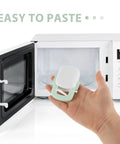 Hand holding Four Pack Childproof Oven Safety Locks For Cabinets And Microwaves Durable ABS Kitchen Locks For Safe Access Easy Install Strong Fixation Prevent Little Hands From Opening Appliances in front of open microwave