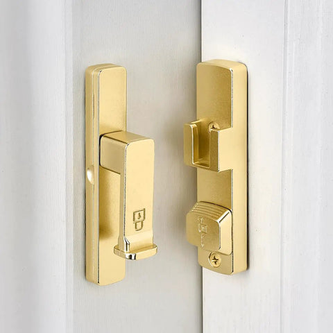 Heavy Duty Gold 90 Degree Barn Door Lock With Flip Gate Latch And Dual Secure Mounting Built Badass For Quick Install and shown on a white door.