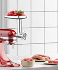 Metal meat grinder attachment for KitchenAid stand mixer; red mixer with chrome grinding head and meat chunks on tray