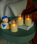 Ivory Flameless Taper Candles With Remote And Timer, Battery Operated LED Candles in glass holders on a green table