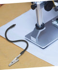 Close-up of adjustable soldering arm with magnifying glass and lamp clamp, showing flexible gooseneck holder on workstation