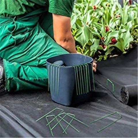 Person using Heavy Duty Garden Stakes And Ground Anchors U Shape Steel Nails for artificial grass, sod, and weed fabric installation.