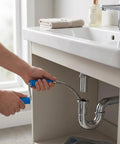 Person using Tough As Nails 3 Meter Drain Auger With Compatible Drill Attachment Flexible Plumbing Snake under a sink.