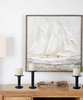 Nautical painting of a sailboat above a wooden table with three black candle holders and white candles.