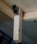 Rock Solid Folding Table Leg Brackets With Self Lock Hinges And Screws For Quick Workbench Upgrades Adjustable Zero To Ninety Degrees Bears Up To Five Hundred Pounds In Clean Matte Black attached to a wooden beam.